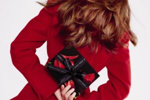 woman in red coat holding a gift wrapped box behind her back