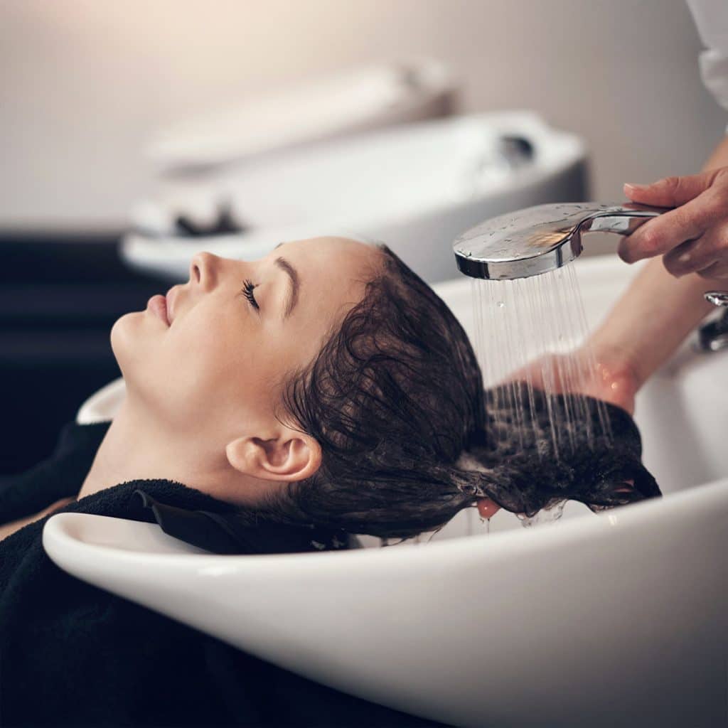 Daybreak salon stylist applying Kerastase professional hair treatment at the shampoo bowl in Woodhaven Michigan