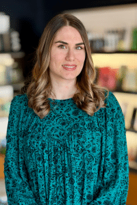 Woodhaven hair stylist specializing in highlights, dimensional blonding and precisions haircuts standing in front of an Aveda haircare display of home care products