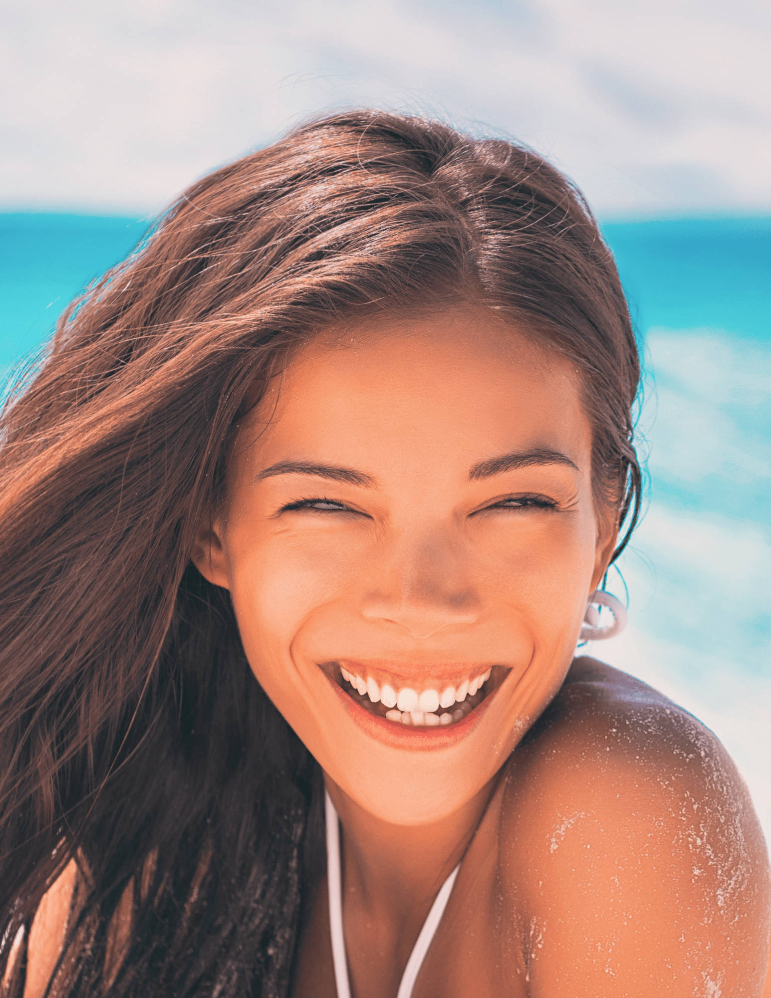 young woman smiling with a glowing facial on a beach