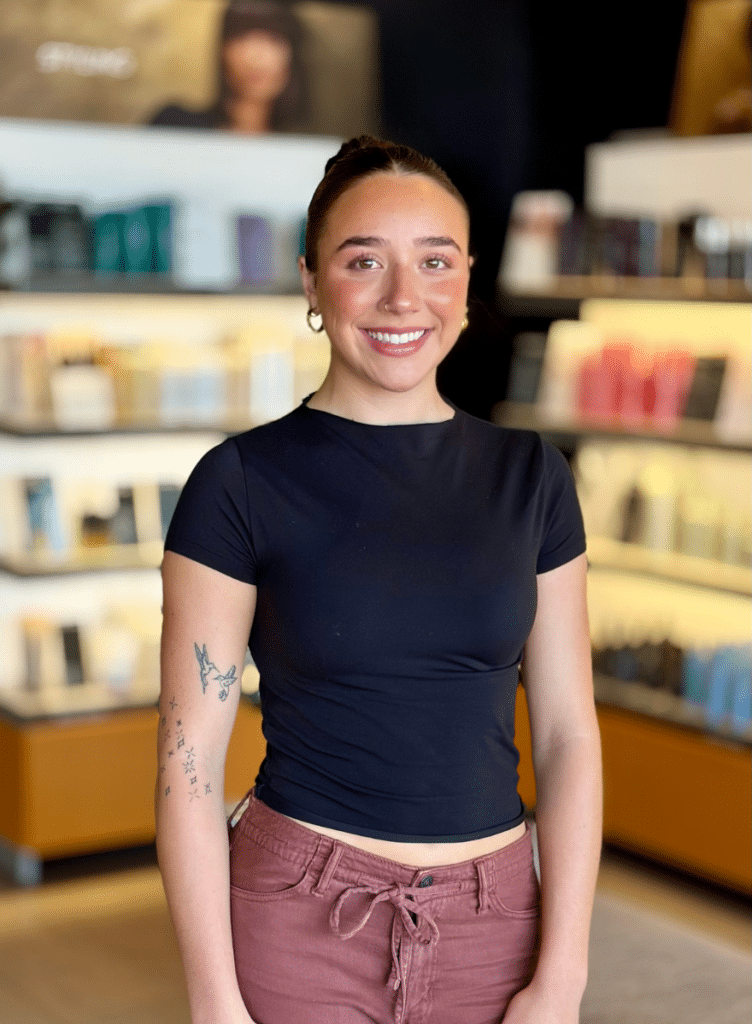 guest service associate standing in front of Aveda retails shelves in a Woodhaven, MI salon retail area