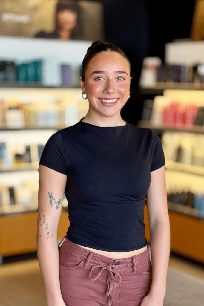 guest service associate standing in front of Aveda retails shelves in a Woodhaven, MI salon retail area