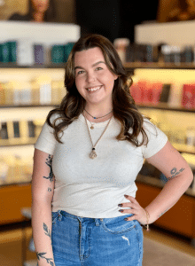 HAIR STYLIST STANDING IN FRONT OF AVEDA HAIR CARE PRODUCTS RETAIL DISPLAY IN WOODHAVEN MI