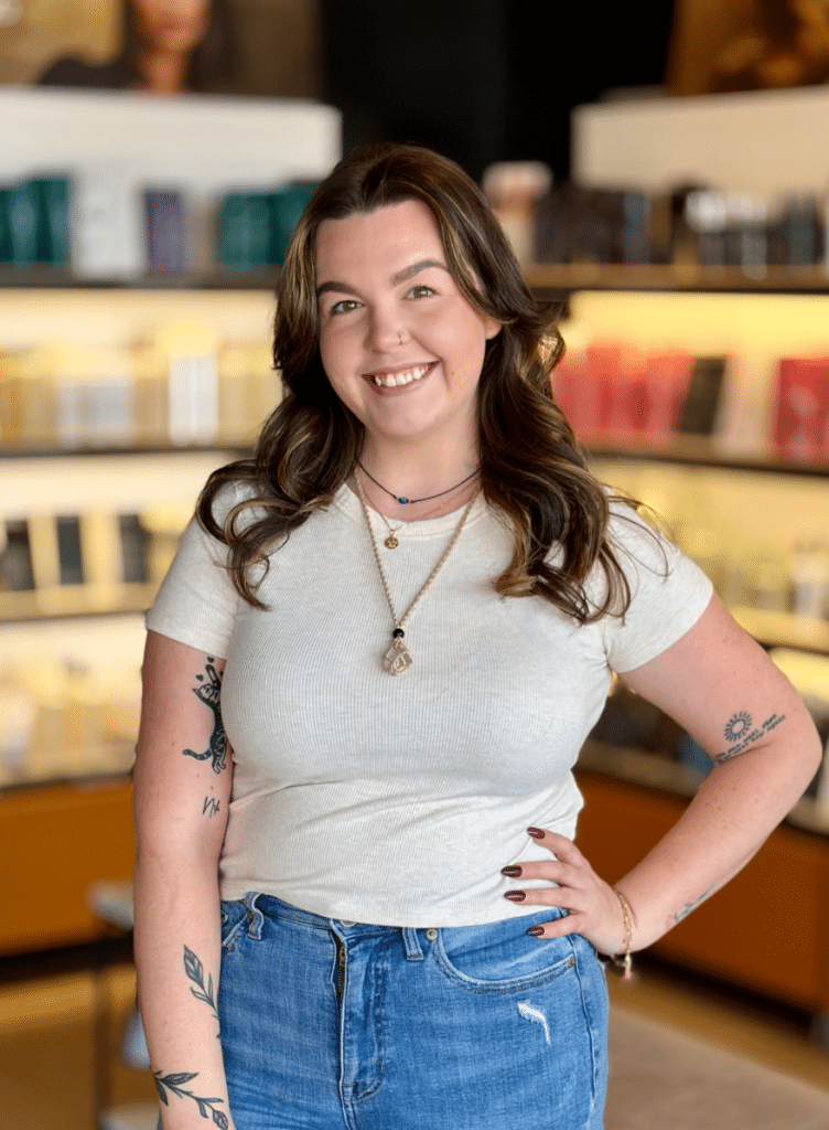 HAIR STYLIST STANDING IN FRONT OF AVEDA HAIR CARE PRODUCTS RETAIL DISPLAY IN WOODHAVEN MI